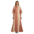 Woman in a tiered maxi dress with a tie-dye print in warm, earthy tones of peach and cream. The dress features flowy sleeves, a ruffled neckline, and a tiered hem.